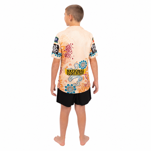 A child shown from the back wearing a short-sleeve collared shirt with a colorful abstract print and black shorts, standing against a plain white background.